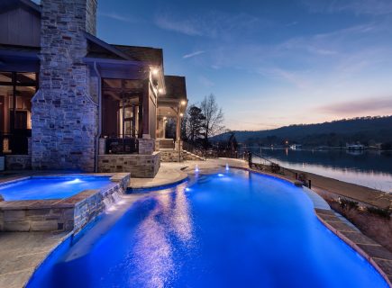 freeform pool with blue lighting overlooking lake at dusk